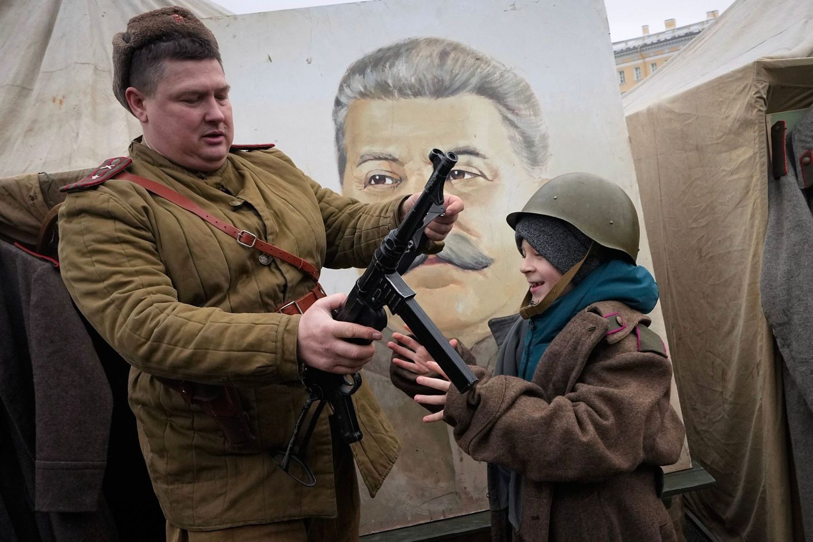 Член исторического клуба в форме времен Второй мировой войны показывает оружие мальчику возле портрета Иосифа Сталина на военно-исторической выставке на Дворцовой площади в Санкт-Петербурге. Экспозиция приурочена к 80-летию со дня снятия блокады Лени