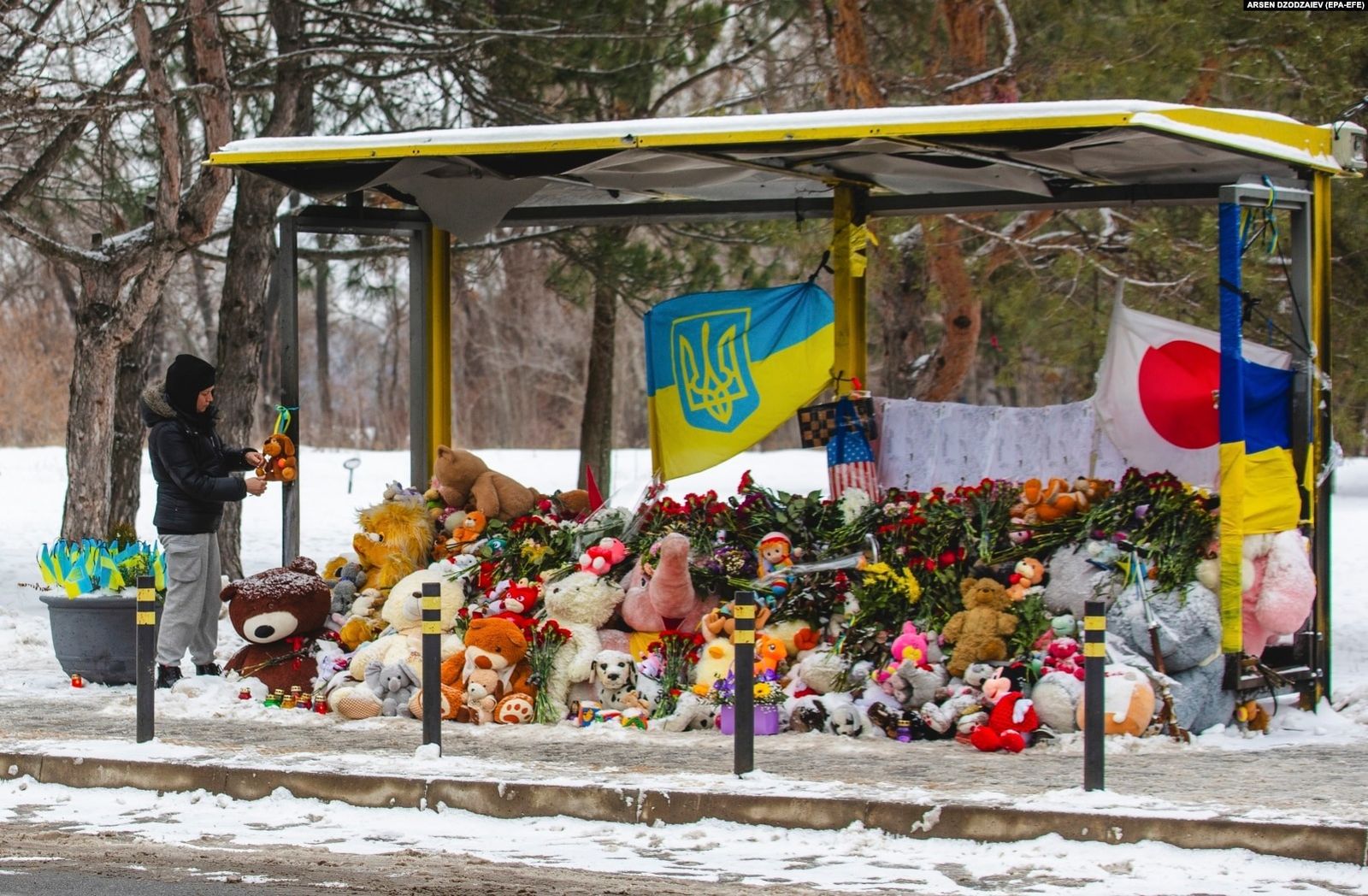 Украинцы возлагают цветы к импровизированным мемориалу на автобусной остановке возле руин жилого дома в Днепре. Год назад по меньшей мере 46 жителей этого района погибли в результате обстрела — посмотрите, как Украина переживала этот страшный месяц, 
