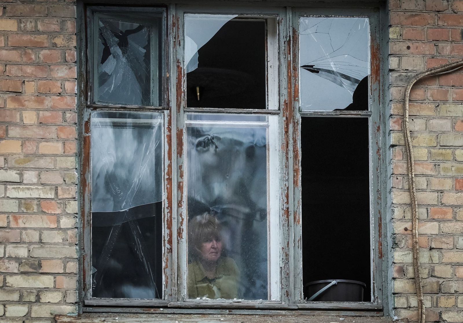 Местная жительница выглядывает из окна своего жилого дома, поврежденного в результате ракетного обстрела Киева. 25 марта / Gleb Garanich / REUTERS