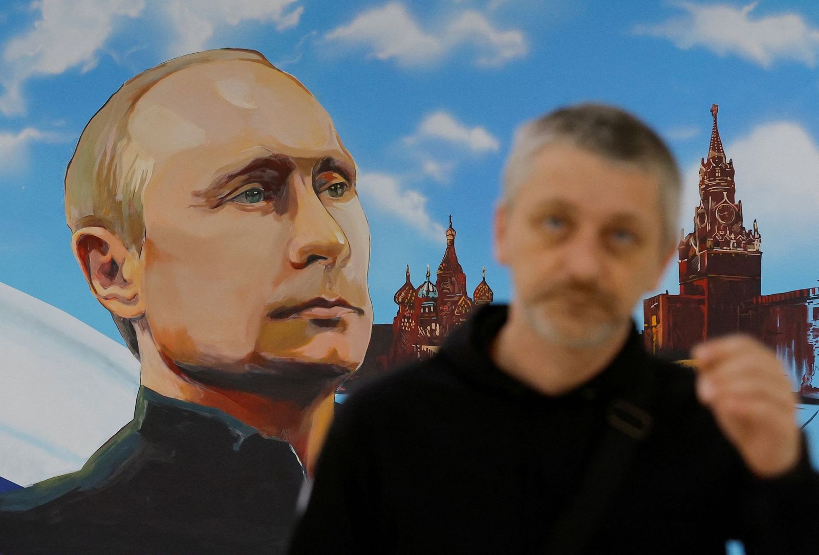 Мужчина идет возле картины с изображением президента России Владимира Путина, собора Василия Блаженного и Спасской башни Московского Кремля на избирательном участке во время местных выборов, проводимых оккупационными властями в Донецке. 8 сентября / 