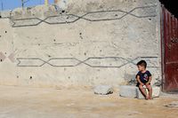 Дети революции. Фоторепортаж из Сирийского Курдистана, Мальчик на фоне стены, изрешеченной пулями — миниатюра
